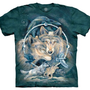 以下が含まれることがあります： 暗いティール色のTシャツ。オオカミ、カラス、天体の要素が描かれた詳細なグラフィック。デザインには、2匹のオオカミの中央画像が含まれており、月の満ち欠けと追加の鳥が描かれた円形のフレームで囲まれています。The Mountainブランドのロゴが見えます。