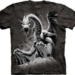 Pode incluir: Uma camiseta preta com uma estampa gráfica branca e cinza de um dragão. O dragão está em pé em uma rocha e tem suas asas abertas. O texto "The Mountain" está impresso na camiseta.