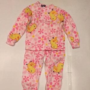 May include: Pink and yellow pajamas with a floral pattern and yellow ducklings. The pajamas are long-sleeved and have a crew neck.