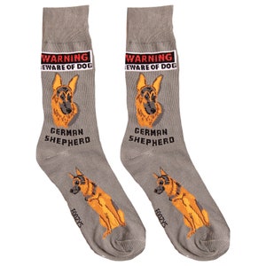 May include: A pair of gray socks with a German Shepherd dog design. The socks have the text "WARNING BEWARE OF DOG" and "GERMAN SHEPHERD" printed on them. The socks are made by the brand "GOOZY'S".