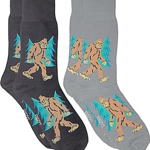 May include: A pair of socks with a Bigfoot design. One sock is gray with a Bigfoot walking through a forest, the other sock is black with a Bigfoot walking through a forest. The socks have the brand name "Foozy's" on the bottom.
