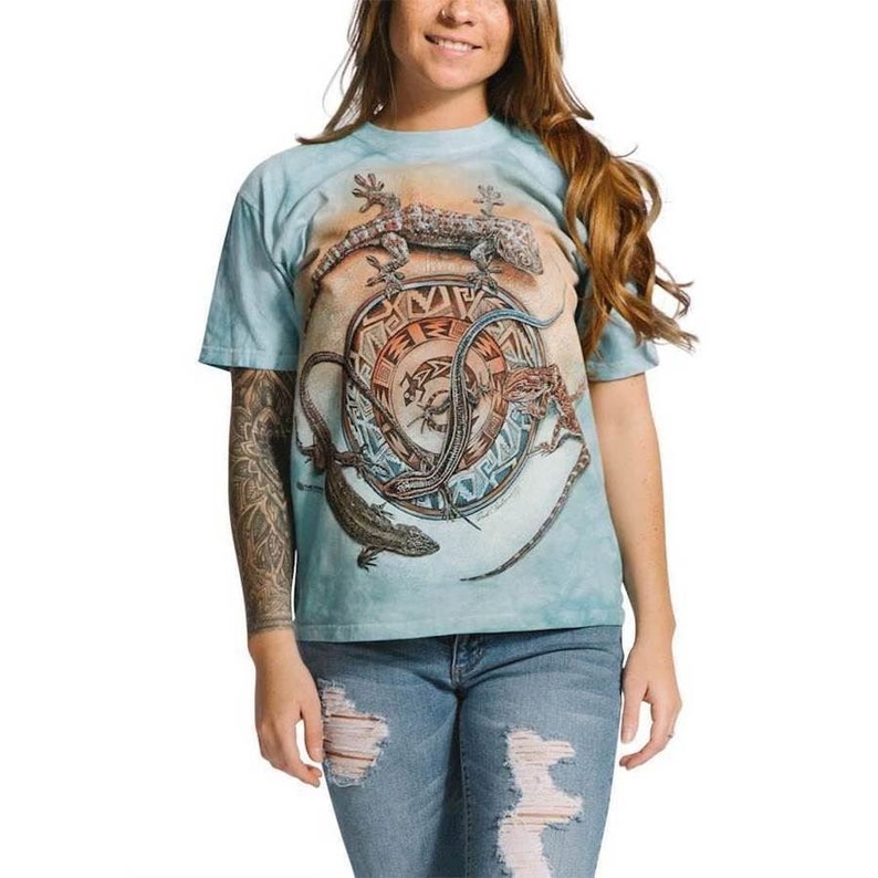 Może przedstawiać: Jasno błękitny t-shirt z efektem tie-dye, przedstawiający okrągły wz&oacute;r z trzema jaszczurkami. Jaszczurki są brązowe, zielone i pomarańczowe. Wz&oacute;r jest otoczony geometrycznym wzorem.