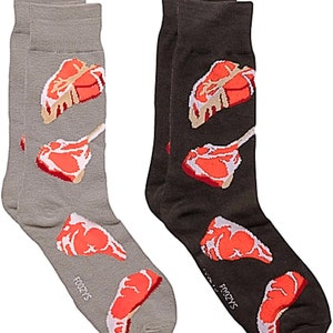 Pode incluir: Um par de meias com um divertido design de comida. Uma meia é cinza com estampas de bife vermelhas e a outra é preta com estampas de bife vermelhas. As meias têm a palavra "Foozys" impressa na parte inferior.