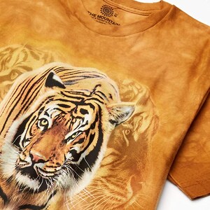 May include: A brown tie-dye t-shirt with a large image of a tiger's face. The shirt has the text "The Mountain" printed on the tag.