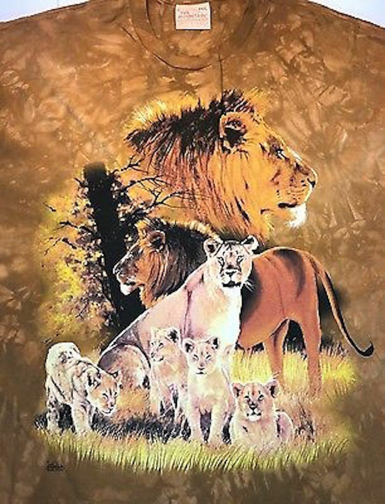 May include: A brown tie-dye t-shirt with a print of a pride of lions in a savanna setting. The lions are in various poses, including a large male lion with a mane, a female lion with cubs, and a group of cubs playing. The background is a brown and tan tie-dye pattern.