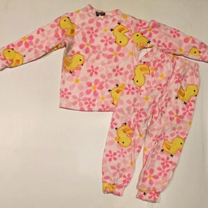 May include: Pink and yellow children's pajamas with a duckling print. The pajamas have long sleeves and long pants.