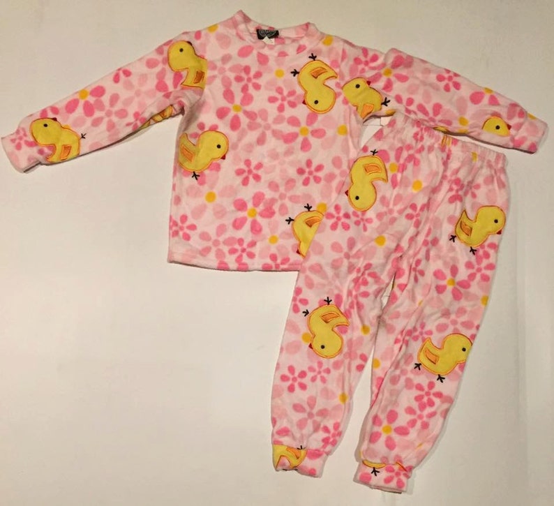 May include: Pink and yellow children's pajamas with a duckling print. The pajamas have long sleeves and long pants.