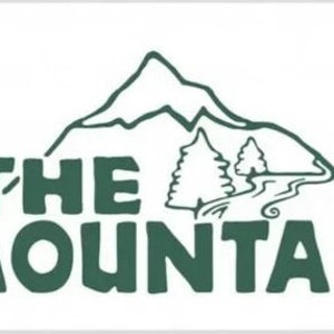 May include: A green logo with the text "THE MOUNTAIN" in a bold, stylized font. A stylized mountain with a winding path and two trees is behind the text. A stylized sun with orange and brown accents is in the upper left corner.