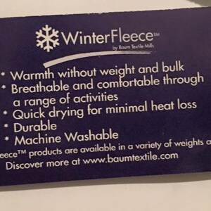 May include: A blue tag with white text describing the features of WinterFleece&trade; by Baum Textile Mills. The tag lists the following features: warmth without weight and bulk, breathable and comfortable, quick drying, durable, and machine washable. The tag also states that WinterFleece&trade; products are available in a variety of weights and styles. The tag includes the website address www.baumtextile.com.