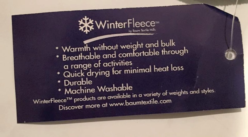 May include: A blue tag with white text describing the features of WinterFleece&trade; by Baum Textile Mills. The tag lists the following features: warmth without weight and bulk, breathable and comfortable, quick drying, durable, and machine washable. The tag also states that WinterFleece&trade; products are available in a variety of weights and styles. The tag includes the website address www.baumtextile.com.