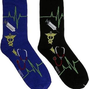 Puede incluir: Un par de calcetines coloridos con un tema médico. Un calcetín es azul con un latido del corazón verde, una jeringa y un símbolo de caduceo. El otro calcetín es negro con un latido del corazón verde, una jeringa y un símbolo de caduceo. Ambos calcetines tienen un estetoscopio rojo y la palabra "FOOZY'S" impresa en ellos.