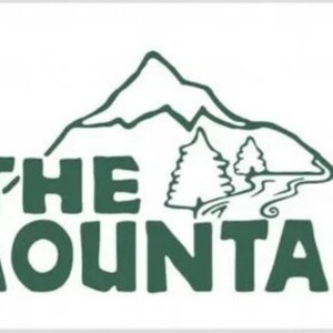 May include: A green logo with the text "THE MOUNTAIN" in a bold, stylized font. A stylized mountain with a winding path and two trees is behind the text. A stylized sun with orange and brown accents is in the upper left corner.