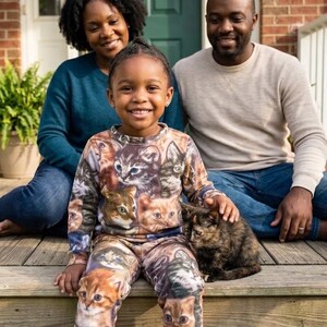 May include: A long-sleeved shirt and matching pants set featuring an all-over photographic print of various cat faces in shades of brown, gray, and white. The garment has a crew neckline and a fitted silhouette, showcasing multiple feline expressions.