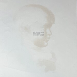 May include: A soft, sepia-toned print of a person's profile, likely a portrait. The image is faded, with the subject's features subtly defined against a white background. Text is visible on the right side of the image.