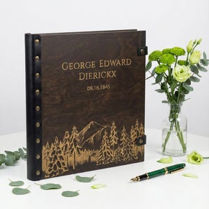 Personalized wooden Photo album perfect for a milestone birthday or retirement gift. The dark wood cover shows a custom engraved name, a 1945 birth year, and a nature-inspired mountain scene.