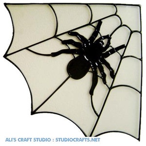 May include: A black spider sits in the centre of a white web with black lines. The web is in the shape of a corner.