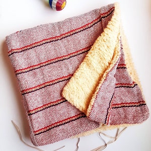 Puede incluir: Una manta de rayas rojas y blancas con un forro de vellón crema suave. La manta está doblada por la mitad y tiene flecos alrededor de los bordes.