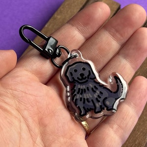 May include: A black and white dog charm keyring with a black metal chain. The charm is made of clear acrylic and features a detailed illustration of a dog.