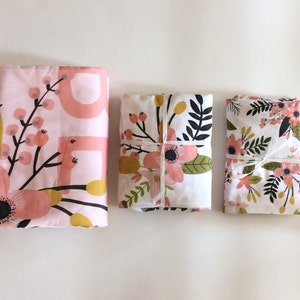 May include: Three fabric squares with floral patterns. The top square is pink with a floral design and white accents. The middle square is white with a pink and green floral design. The bottom square is white with a pink and green floral design.