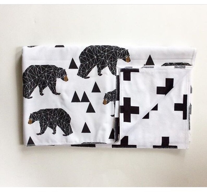 May include: A black and white geometric patterned baby blanket with a black bear design on one side and a black plus sign design on the other side.