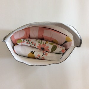 May include: A white fabric storage bag with a grey top, filled with pink and white floral patterned fabric. The fabric is folded and stacked inside the bag.
