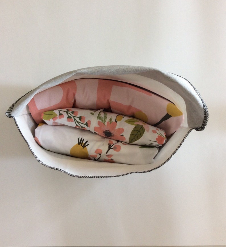 May include: A white fabric storage bag with a grey top, filled with pink and white floral patterned fabric. The fabric is folded and stacked inside the bag.