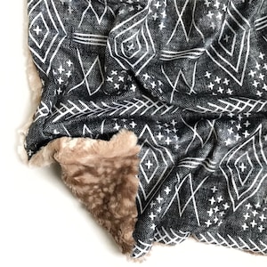 May include: A black and white patterned throw blanket with a soft, brown faux fur lining. The blanket features a geometric design with diamonds and stars.