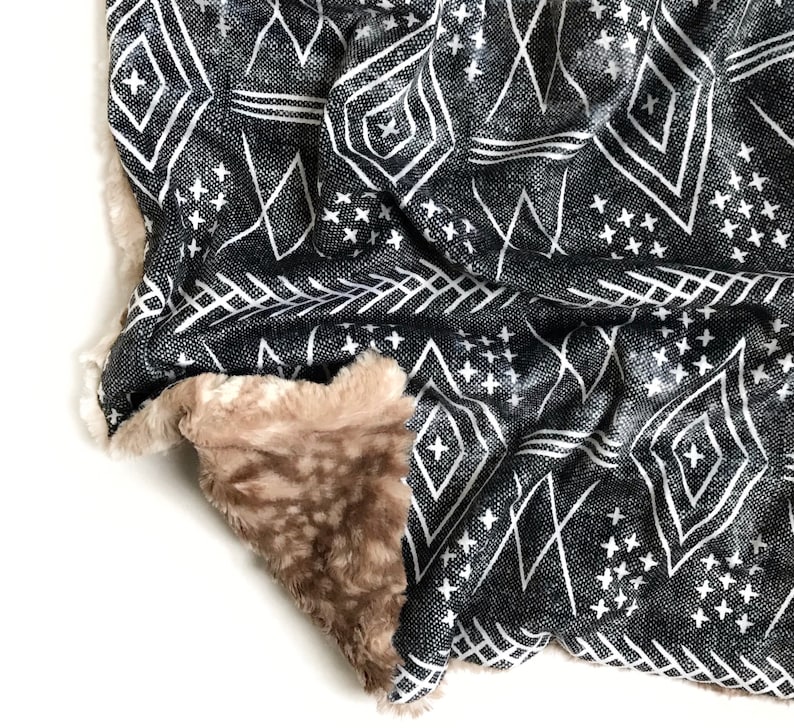 May include: A black and white patterned throw blanket with a soft, brown faux fur lining. The blanket features a geometric design with diamonds and stars.