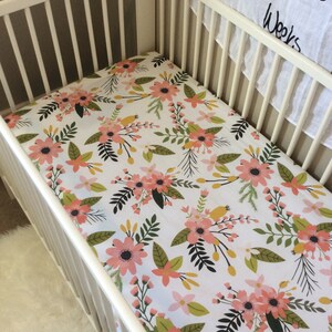 May include: White cot with a floral cot sheet featuring pink, green and yellow flowers on a white background.