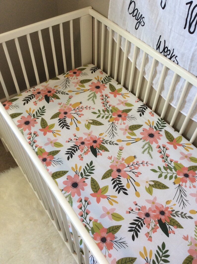 May include: White cot with a floral cot sheet featuring pink, green and yellow flowers on a white background.