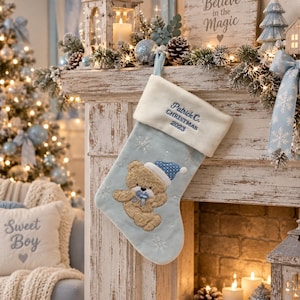 May include: A light blue Christmas stocking with a white plush cuff featuring the embroidered text Patrick C. CHRISTMAS 2023. The stocking displays a tan teddy bear wearing a blue polka dot hat and a blue bow, accented with white snowflake patterns.