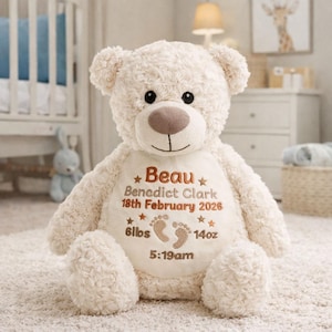 Könnte beinhalten: Ein cremefarbener Plüsch-Teddybär mit weicher, lockiger Textur. Der Bär hat einen glatten Bauchfleck, der mit dem Namen Beau Benedict Clark, dem Datum 18. Februar 2026, dem Gewicht 6lbs 14oz und der Uhrzeit 5:19 Uhr bestickt ist.