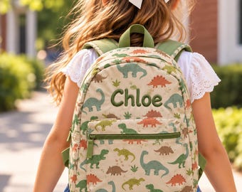 May include: A beige backpack featuring a repeating pattern of green and orange dinosaurs. The front pocket displays the name Chloe embroidered in dark green thread. The bag includes olive green straps and a matching top handle for carrying.