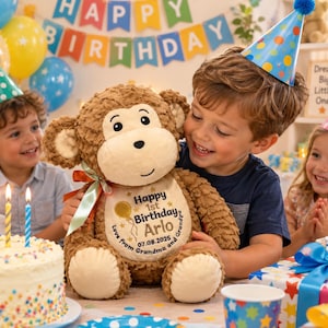 May include: A brown plush monkey toy with a cream-colored face and belly. The belly features embroidered text reading Happy 1st Birthday Arlo, 07.08.2025, Love from Grandma and Grandpa, with a gold balloon graphic. A light green ribbon is tied at the neck.