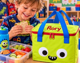 May include: A lime green insulated lunch bag featuring a monster face with large white eyes and black teeth, blue carrying handles, a red zipper, and the name Rory embroidered in red thread on the top lid of the rectangular container.