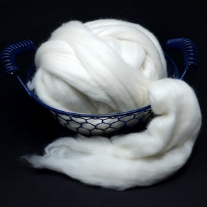 Puede incluir: Una bola de lana blanca y esponjosa en una cesta de alambre azul. La lana se derrama de la cesta.