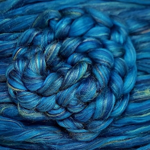 May include: A close-up of teal blue fibre with a braided swirl in the centre. The fibre is soft and fluffy, and it has a subtle shimmer.