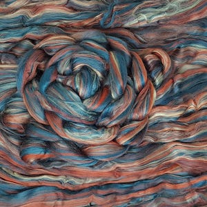 May include: A close-up of a bundle of colourful yarn in shades of blue, orange, and white. The yarn is arranged in a swirling pattern, creating a textured and abstract design.
