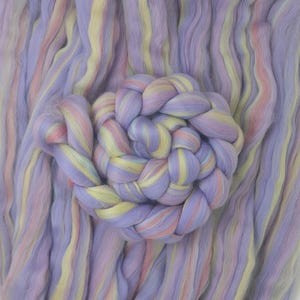 Puede incluir: Primer plano de un paquete de vellón de lana de colores en tonos de morado, rosa, amarillo y blanco. El vellón está dispuesto en un patrón trenzado.