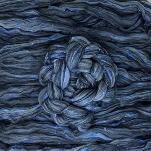 May include: A close-up of a blue and grey fibre blend, with a braided section in the centre. The fibre is soft and fluffy, and has a subtle shimmer.