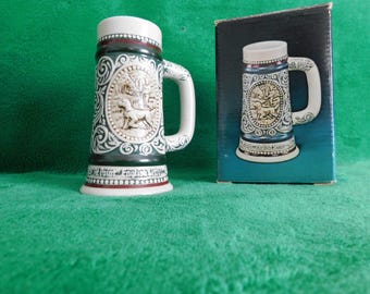 Puede incluir: Una jarra de cerveza de cerámica con asa y tapa blancas, con un diseño en relieve detallado. La jarra tiene una combinación de colores verde oscuro y blanco con un relieve ovalado central que representa un perro. La base dice "Old Point English Edition."
