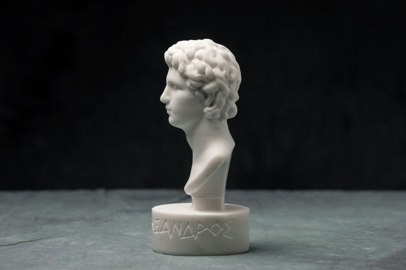 May include: A white marble bust of a man with curly hair, in profile. The bust is mounted on a circular base with the Greek inscription "&Lambda;&Epsilon;&Alpha;&Nu;&Delta;&Rho;&Omicron;&Sigma;". The sculpture is set against a dark background.