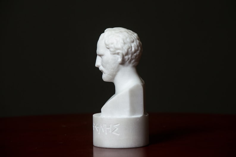 Puede incluir: Busto de m&aacute;rmol blanco de un hombre con barba, sobre una base de m&aacute;rmol blanco con la palabra "HOMERO" inscrita en letras griegas.