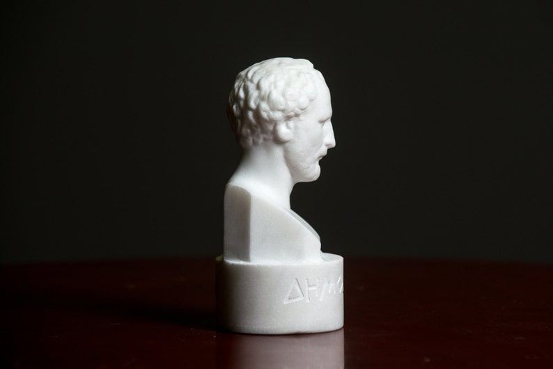 Puede incluir: Busto de m&aacute;rmol blanco que representa la cabeza y los hombros de un hombre. El busto est&aacute; sobre un pedestal con la palabra "&Delta;&Eta;&Mu;&Omicron;" inscrita en la parte delantera.