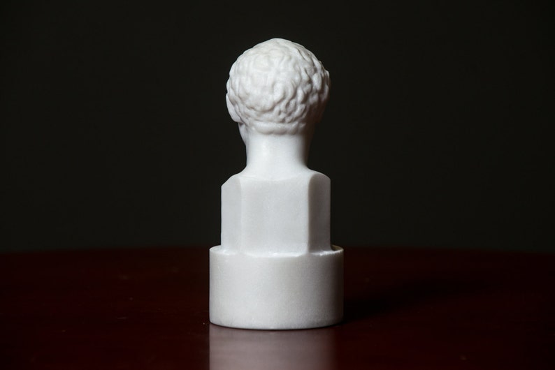 Puede incluir: Busto de m&aacute;rmol blanco de una persona con el pelo corto. El busto est&aacute; sobre una base redonda blanca.