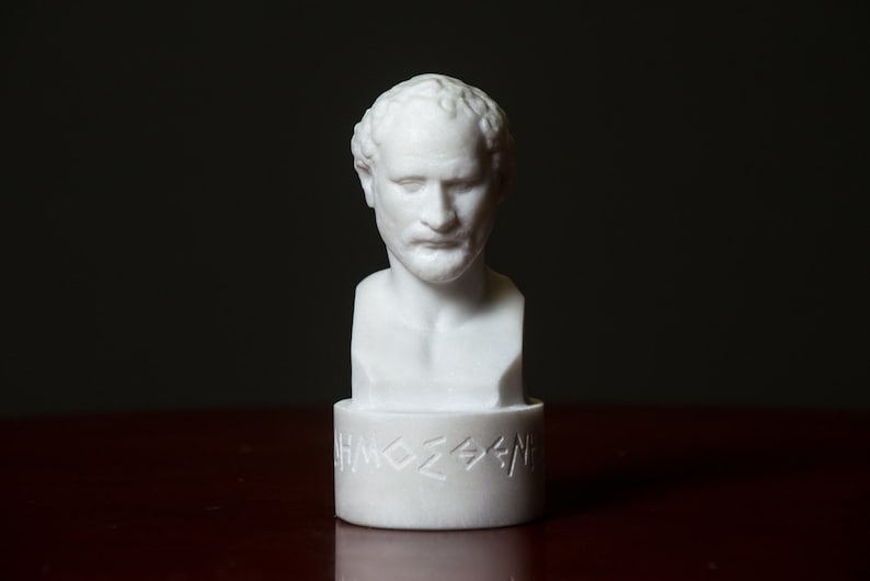 Puede incluir: Busto de m&aacute;rmol blanco de un hombre con el pelo corto y barba. El busto est&aacute; sobre una base blanca con letras griegas.