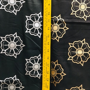May include: Black fabric with a repeating pattern of gold and white stylized flowers. A yellow measuring tape is on the right side of the image.