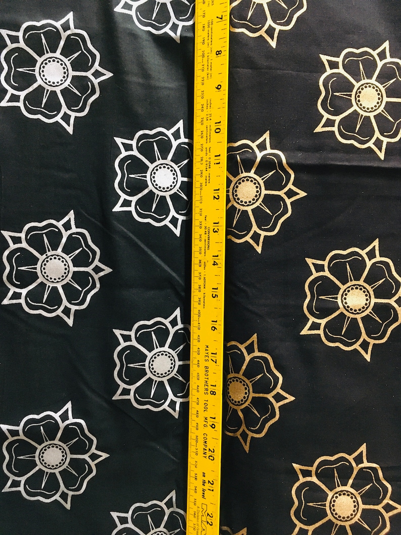 May include: Black fabric with a repeating pattern of gold and white stylized flowers. A yellow measuring tape is on the right side of the image.