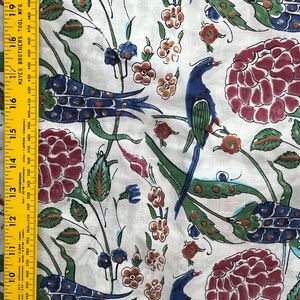 May include: White fabric with a repeating pattern of stylized peacocks, flowers, and leaves. The peacocks are blue, green, and gold. The flowers are red, orange, and yellow. The leaves are green.