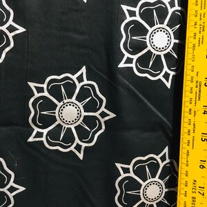 May include: Black fabric with a white repeating pattern of stylized flowers. The fabric is measured with a yellow ruler.